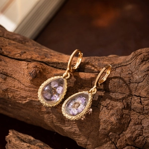 Macro detail of teardrop glass earrings with purple dried flowers on dark wood background