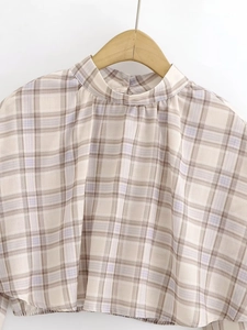 Detailed view of plaid chiffon top with stand collar and elastic hem on a wooden hanger