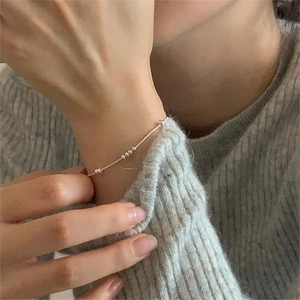 Close-up of minimalist silver snake chain bracelet with beads on a gray knit sweater