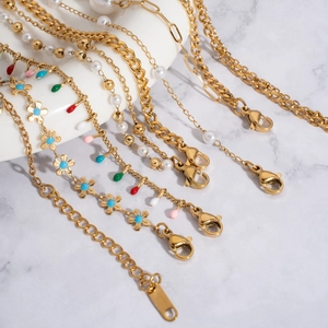 Detail of gold-plated layered pearl anklets with colorful flower pendants on marble backdrop
