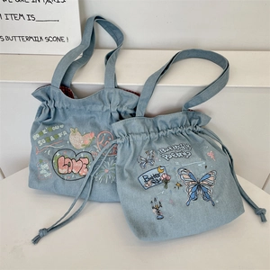 Detail of embroidered butterflies and flowers on light blue denim drawstring tote bag