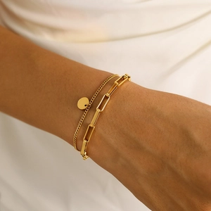 Close-up of double-layer gold titanium bracelets with a round pendant and paperclip chain