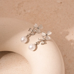 Vue détaillée de boucles d'oreilles fleurs avec pétales en œil de chat et perles blanches