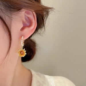 Detailed close-up of sunflower earrings with gold plating and small pearls on a model