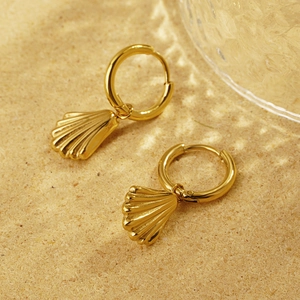 Detail view of 18K gold shell drop earrings on a sandy background with elegant light ripples