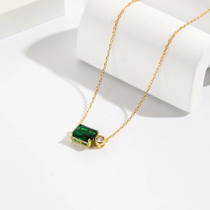 Detailed shot of gold necklace with emerald-cut green stone and clear round diamond