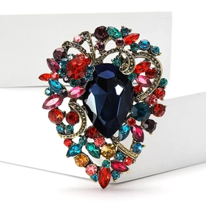 Close-up of vintage gold alloy brooch with deep blue teardrop crystal and colorful rhinestones