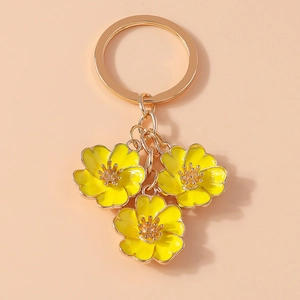 Macro view of golden keychain with three yellow enamel flower pendants on pink background