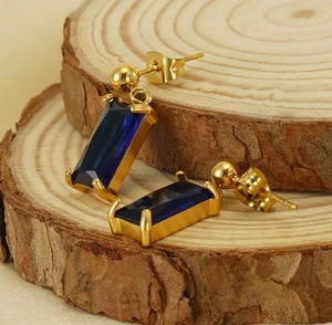 Detailed shot of gold earrings with rectangular blue zircon stones on a wooden base