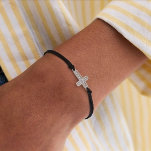 Macro detail of silver cross pendant with crystals on black cord bracelet on wrist