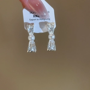 Dettaglio di orecchini a pieghe in argento con inserto in perla bianca e metallo