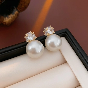 Macro detail of elegant gold-tone earrings with large white pearl and faceted zircon