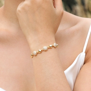 Close-up of golden beaded bracelet with micro-pave zircon charms on a female wrist