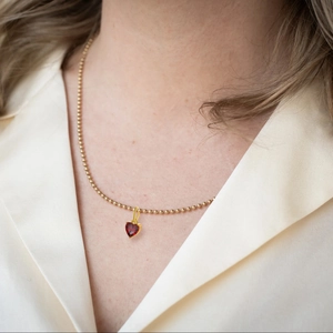 Elegant gold beaded necklace featuring a delicate heart pendant with a vibrant red zircon stone