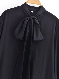 Detail of elegant black long-sleeve blouse featuring a large decorative neck bow tie
