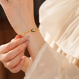 Close-up of a gold-plated pearl bracelet with black enamel hearts on a woman's wrist