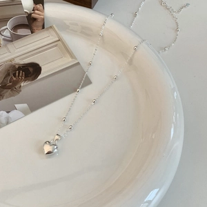 Detail of silver heart pendant necklace with polished bead chain on white ceramic plate