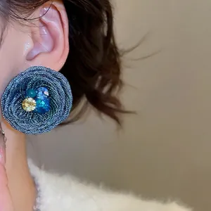 Blue spiral woven earrings with colorful gemstones worn by a model in a close-up profile shot