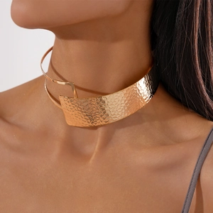 Close-up of hammered gold metal choker with double-layer asymmetrical fold texture