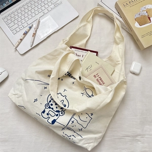 Flat lay of cream canvas tote bag with space astronaut print among laptop and books