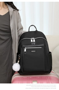 Modern black commuter backpack with a white pompom charm placed on pink luggage