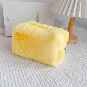 Detailed view of the bright yellow plush makeup bag with zipper on a textured white mat