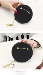 Detail of a black circular coin purse with gold cat ear decor and key ring holder