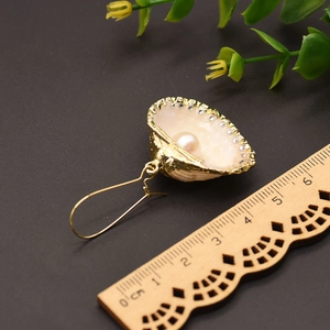 Detail view of a gold shell pearl earring with rhinestones next to a measuring scale