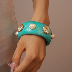 Detail of turquoise resin cuff bracelet featuring golden shell and pearl decorations