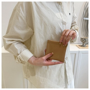 Close-up of minimalist khaki leather clutch bag held by hand in a cozy lifestyle setting