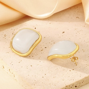 Détail de boucles d'oreilles dorées en acier et résine crème sur fond de soie