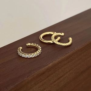 Macro detail of gold-plated twisted ear cuff and sparkling C-shaped zirconia clip earring