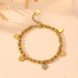 Golden stainless steel heart charm bracelet with paved rhinestones on warm background