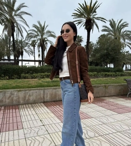 Outdoor full body view of a women's brown suede cropped jacket with denim pants