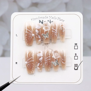 Close-up of handmade press-on nails with butterfly charms and pearl accents on a size card