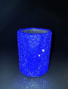 Close-up of a blue rhinestone-encrusted cylindrical makeup brush holder on black background