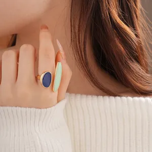 Golden double-stone ring with blue and green oval stones worn on a person's finger