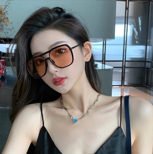 Close-up of oversized square sunglasses with orange lenses and heart pendant necklace