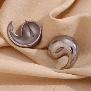 Macro shot of silver irregular water drop earrings on smooth beige silk fabric