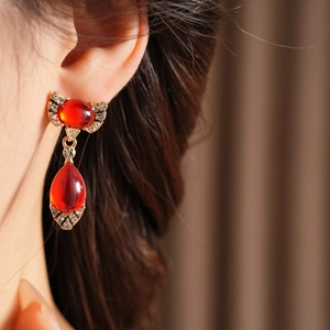 Detail shot of vintage style gold earring featuring a red teardrop gem and rhinestones