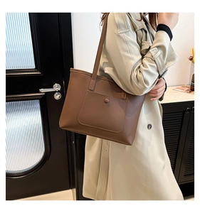 Brown faux leather tote bag with large front pocket styled on a beige trench coat