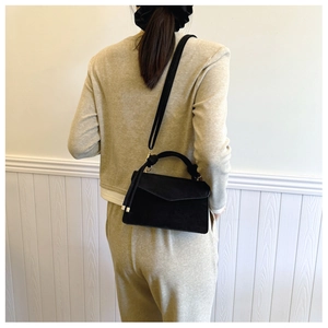 Detail of black faux suede crossbody bag with gold hardware worn by model