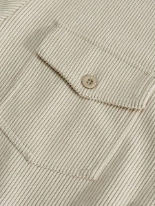 Macro detail of beige corduroy shirt showing flap pocket and premium button texture