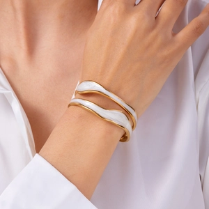 Detail of a wavy gold stainless steel bangle with white enamel inlay on a woman's wrist