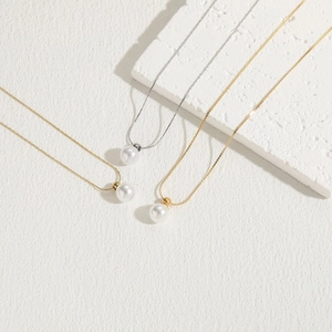 Titanium steel necklaces with white pearls in gold and silver finishes on a textured stone