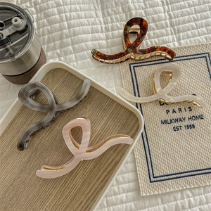 Flat lay of four acetate hair claws in tortoise, black, cream, and pink for thick hair