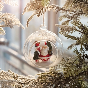 Clear glass Christmas ball ornament with Santa Claus hanging on a snow-covered pine branch