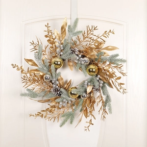 Couronne de Noël avec feuilles dorées, pin givré et boules décoratives sur porte blanche