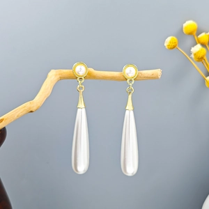 Close-up of elegant long teardrop pearl earrings with golden metal frames on wooden branch