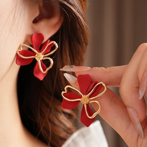 Detail of red flower earrings with gold edges worn by a model in a close-up portrait